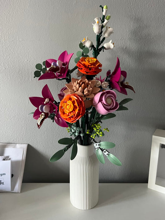Colorful artificial flowers in a white vase against a gray wall.