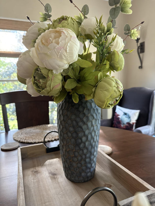 Decorative floral arrangement in a textured vase on a wooden table.