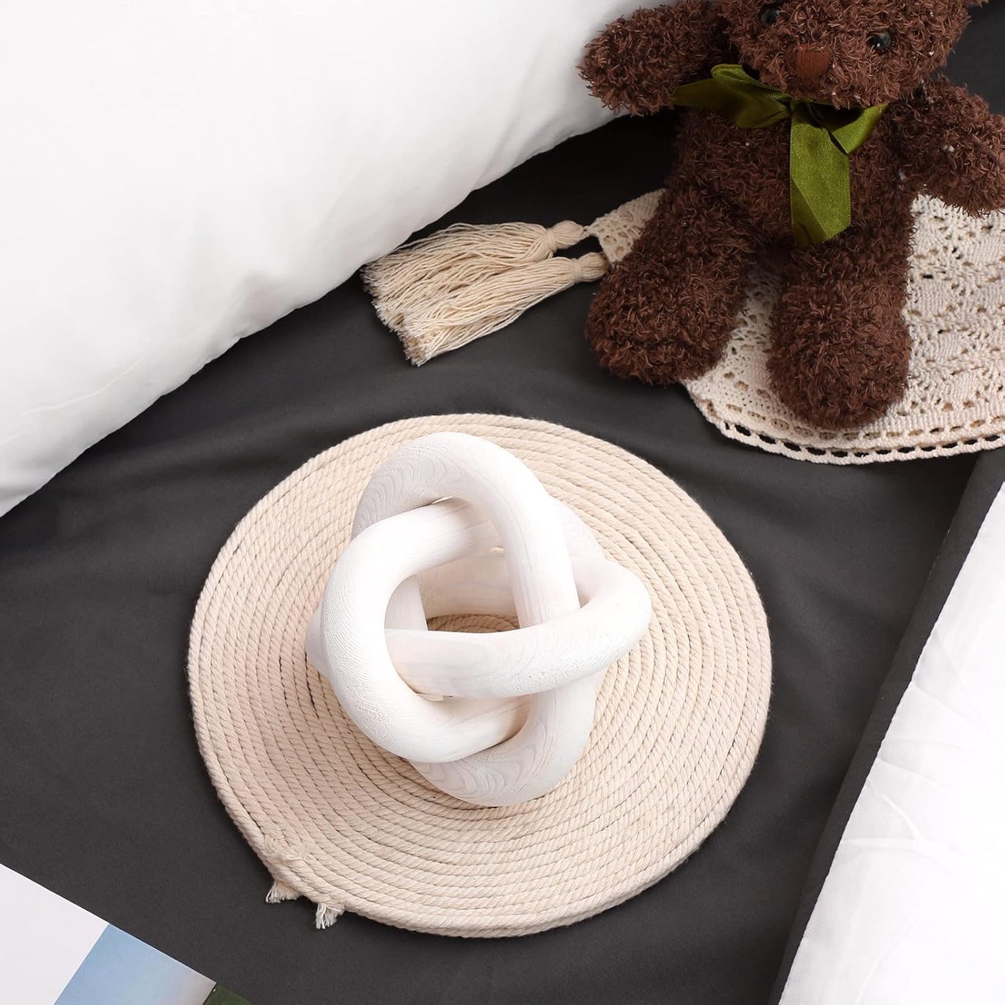 knot sculpture near White knitted scarf on a beige woven plate with a brown teddy bear on a black surface.