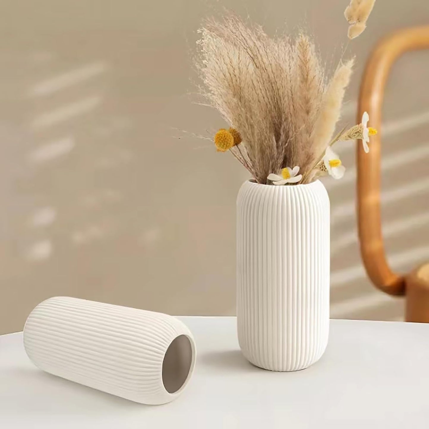 White ribbed vase with dried plants on a light surface with a blurred background