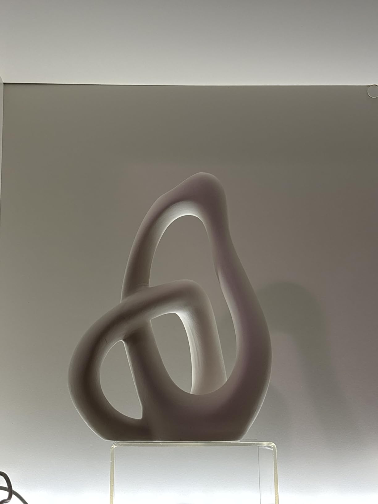 Abstract sculpture on a clear stand against a plain background