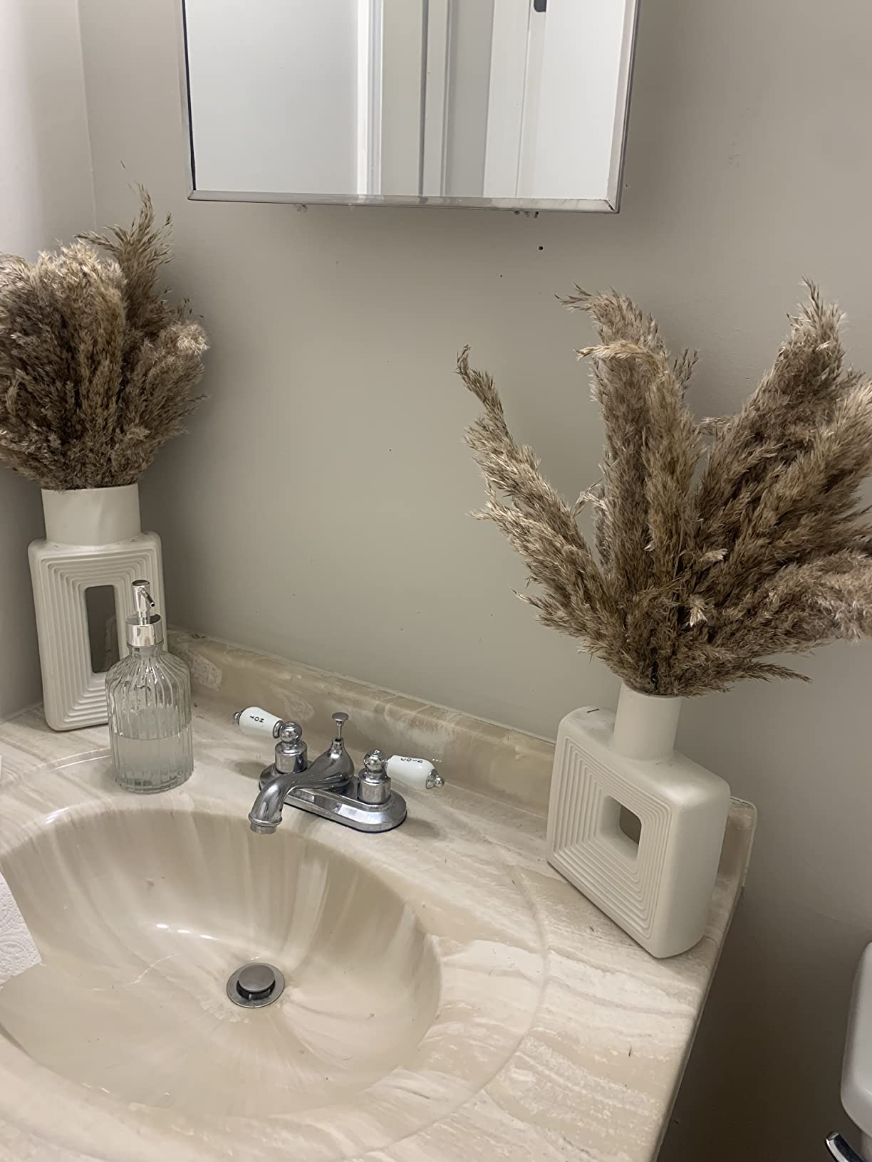 Bathroom sink with decorative vases containing dried plants and a mirror above.