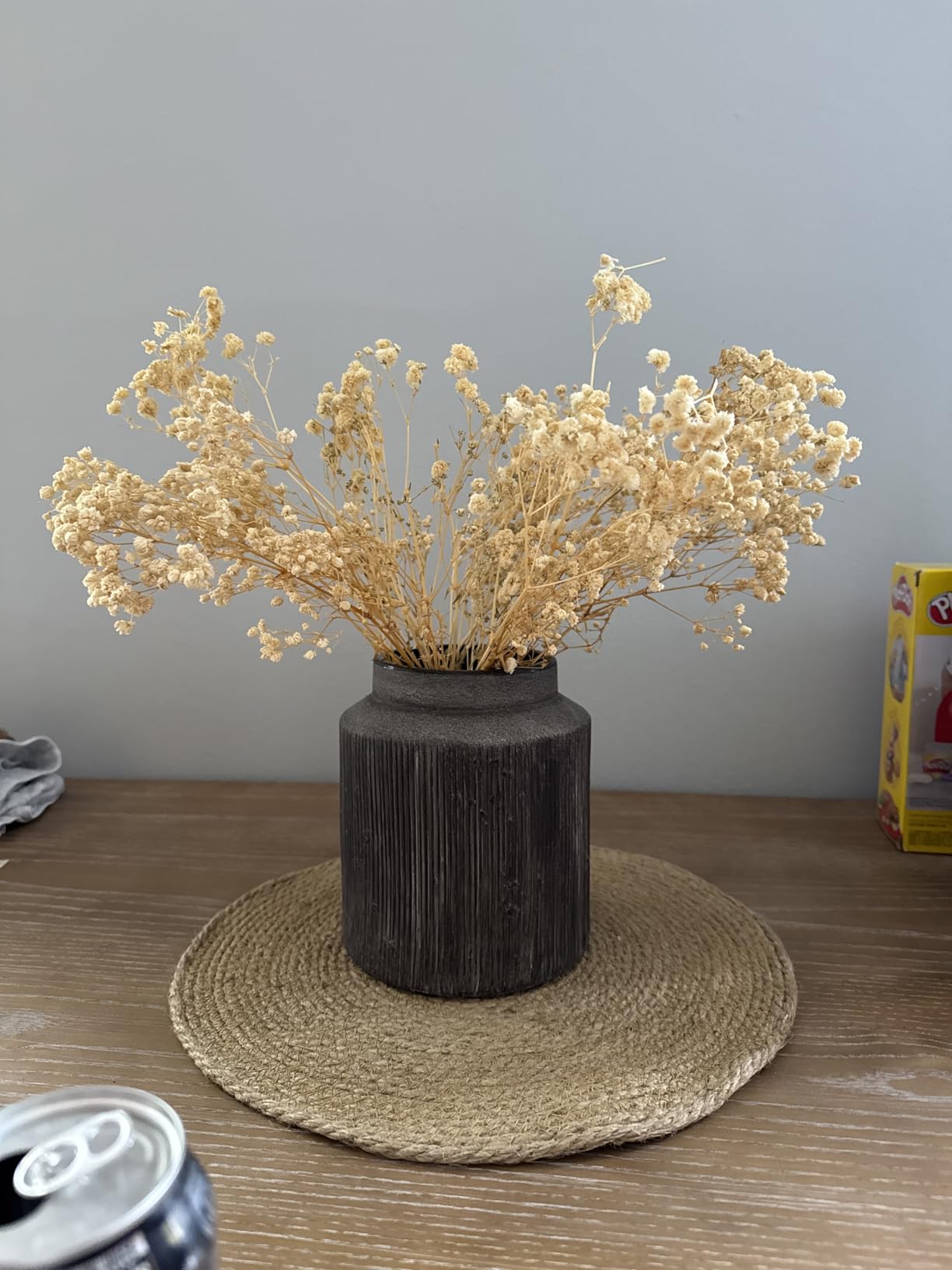 Black vase with dried flowers on a woven mat on a wooden table