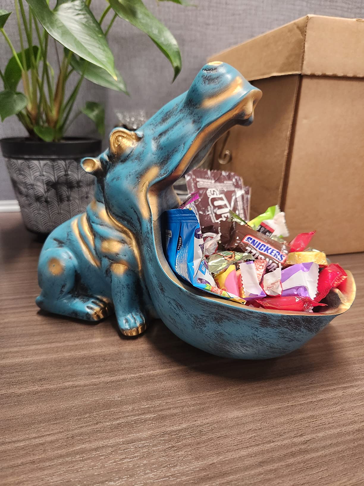 Blue hippo-shaped candy dish filled with colorful candies on a wooden surface.