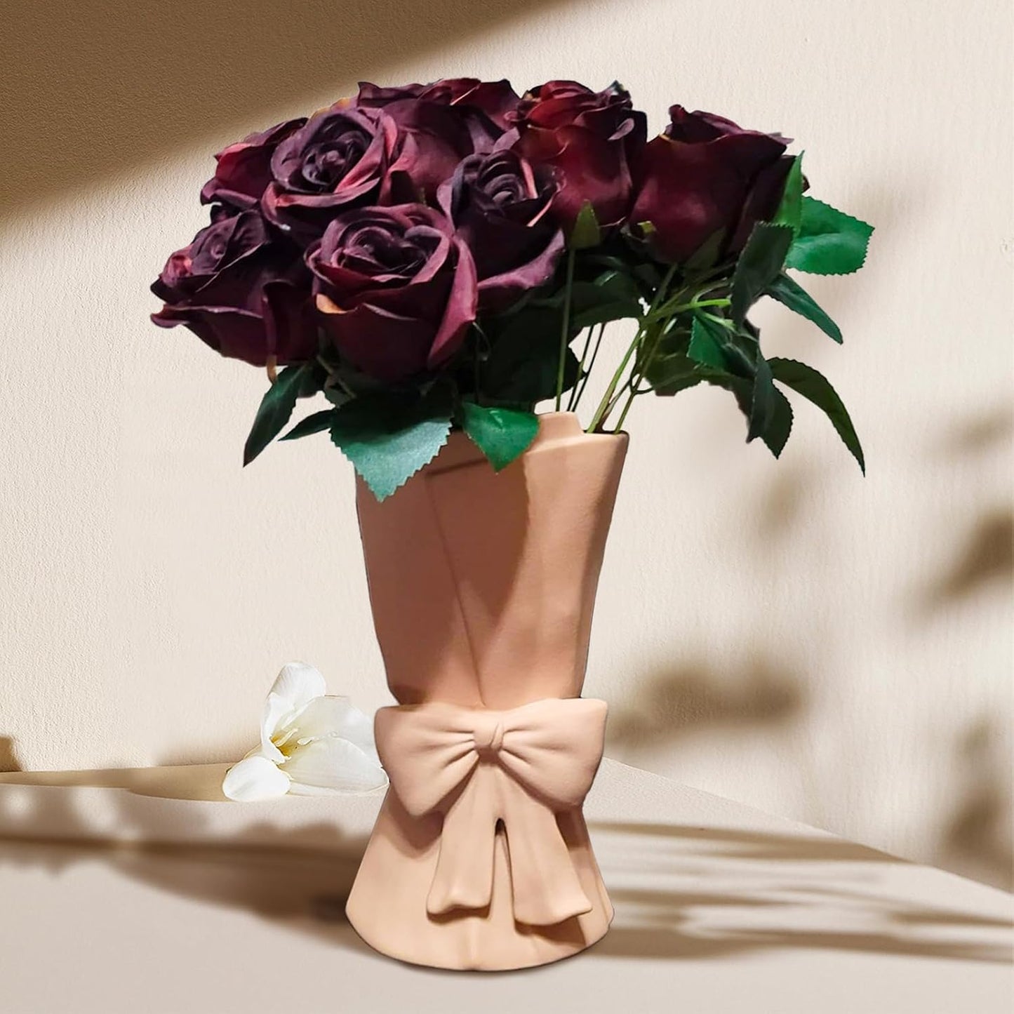 Bouquet of dark purple roses in a beige vase with a bow on a beige background