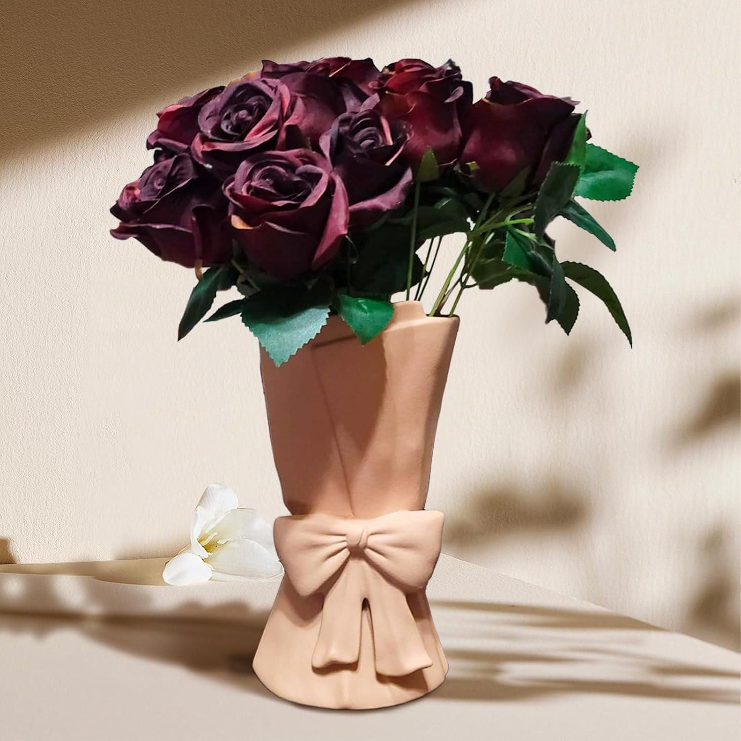 Bouquet of dark purple roses in a beige vase with a bow on a beige background