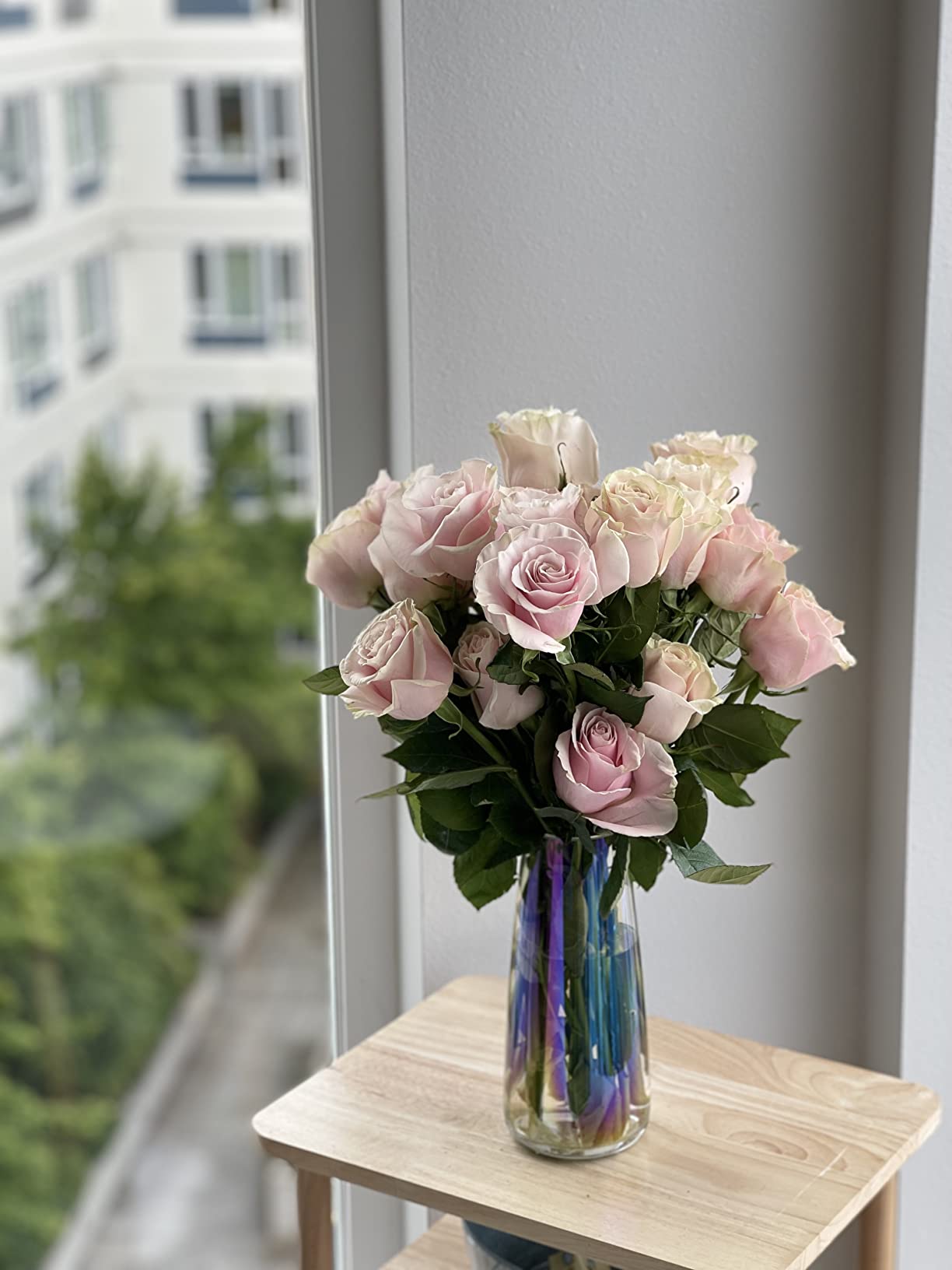 Bouquet of pink roses in a clear vase on a wooden table with a cityscape background