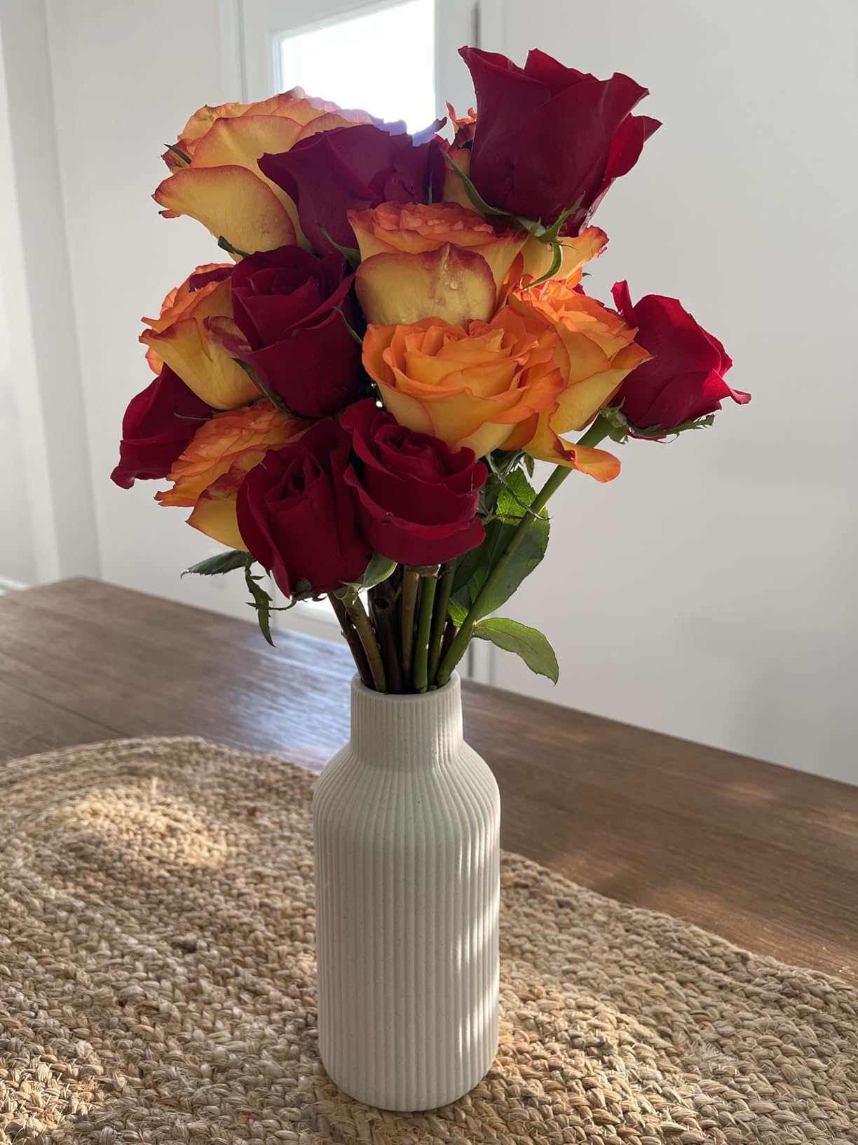 Bouquet of red and orange roses in a white vase on a textured surface.