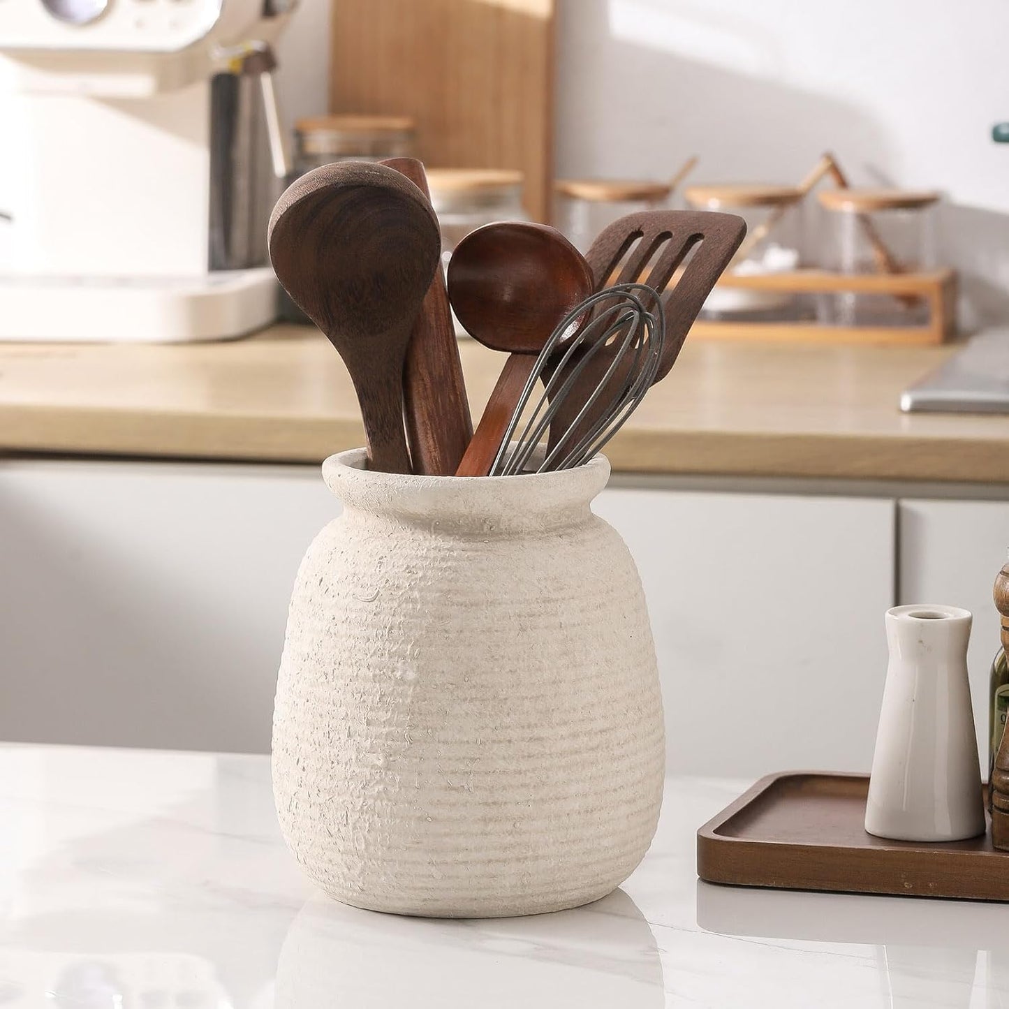 Ceramic utensil holder with wooden and metal utensils on a kitchen counter.