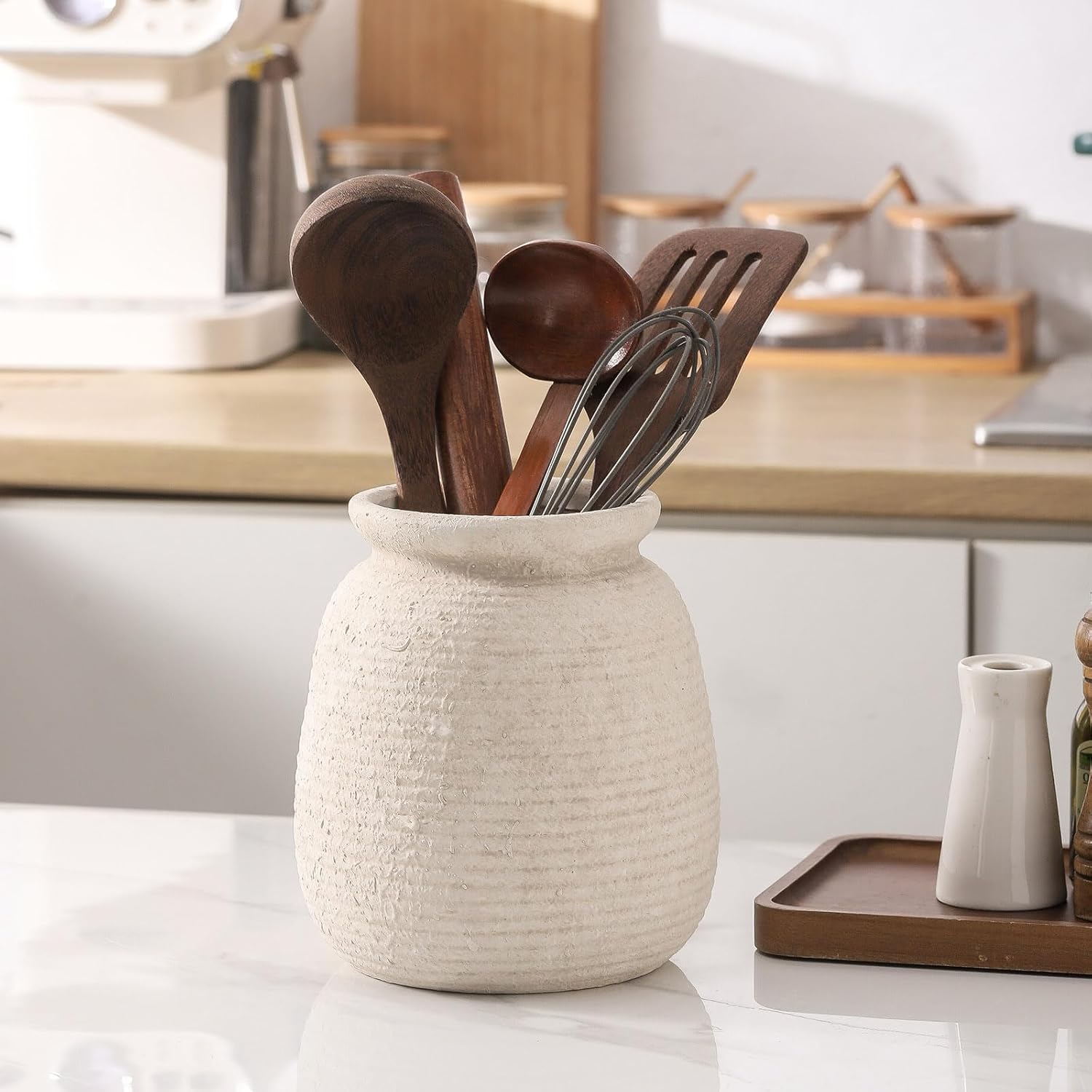 Ceramic utensil holder with wooden and metal utensils on a kitchen counter.
