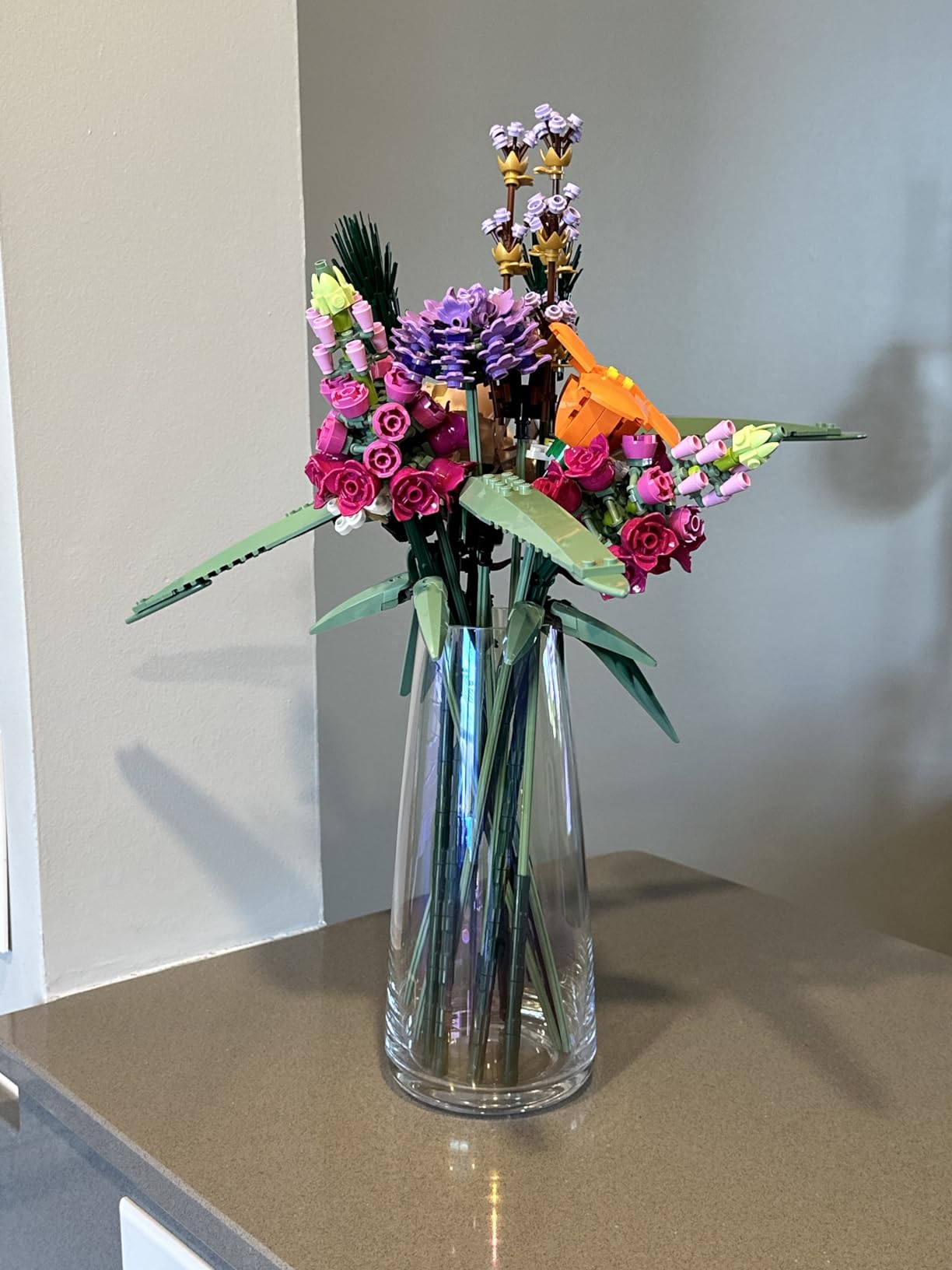 Clear glass vase with colorful artificial flowers on a reflective surface.