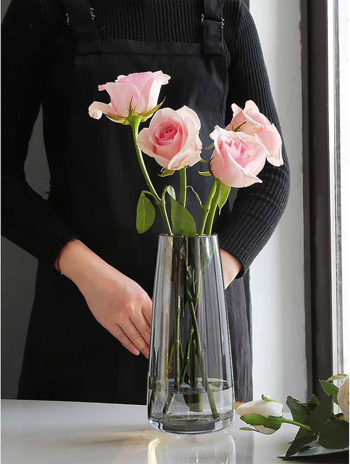 Clear glass vase with pink roses held by a person wearing a black apron.