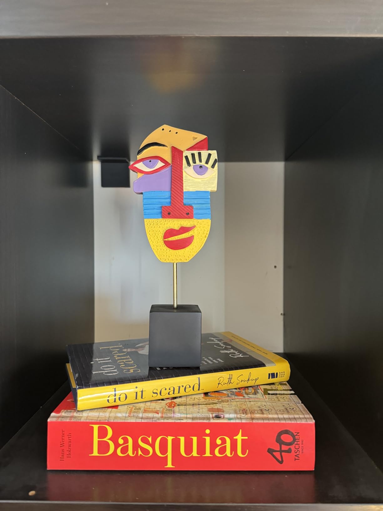 Colorful abstract face sculpture on a stack of books with 'Basquiat' visible