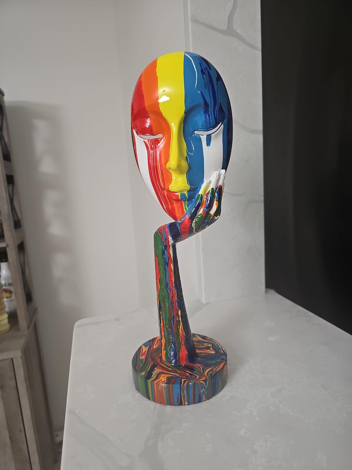 Colorful abstract sculpture of a face on a stand against a white wall.