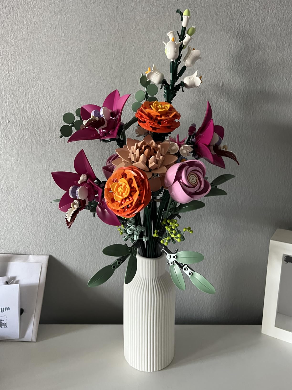 Colorful artificial flowers in a white vase against a gray wall.
