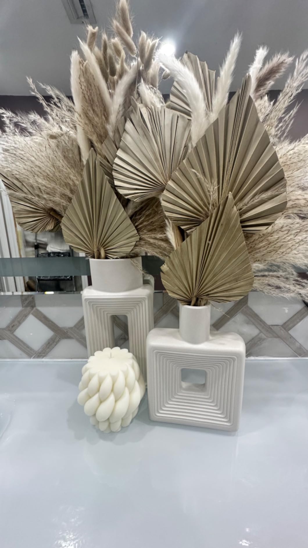 Decorative arrangement with dried plants in white vases on a reflective surface.