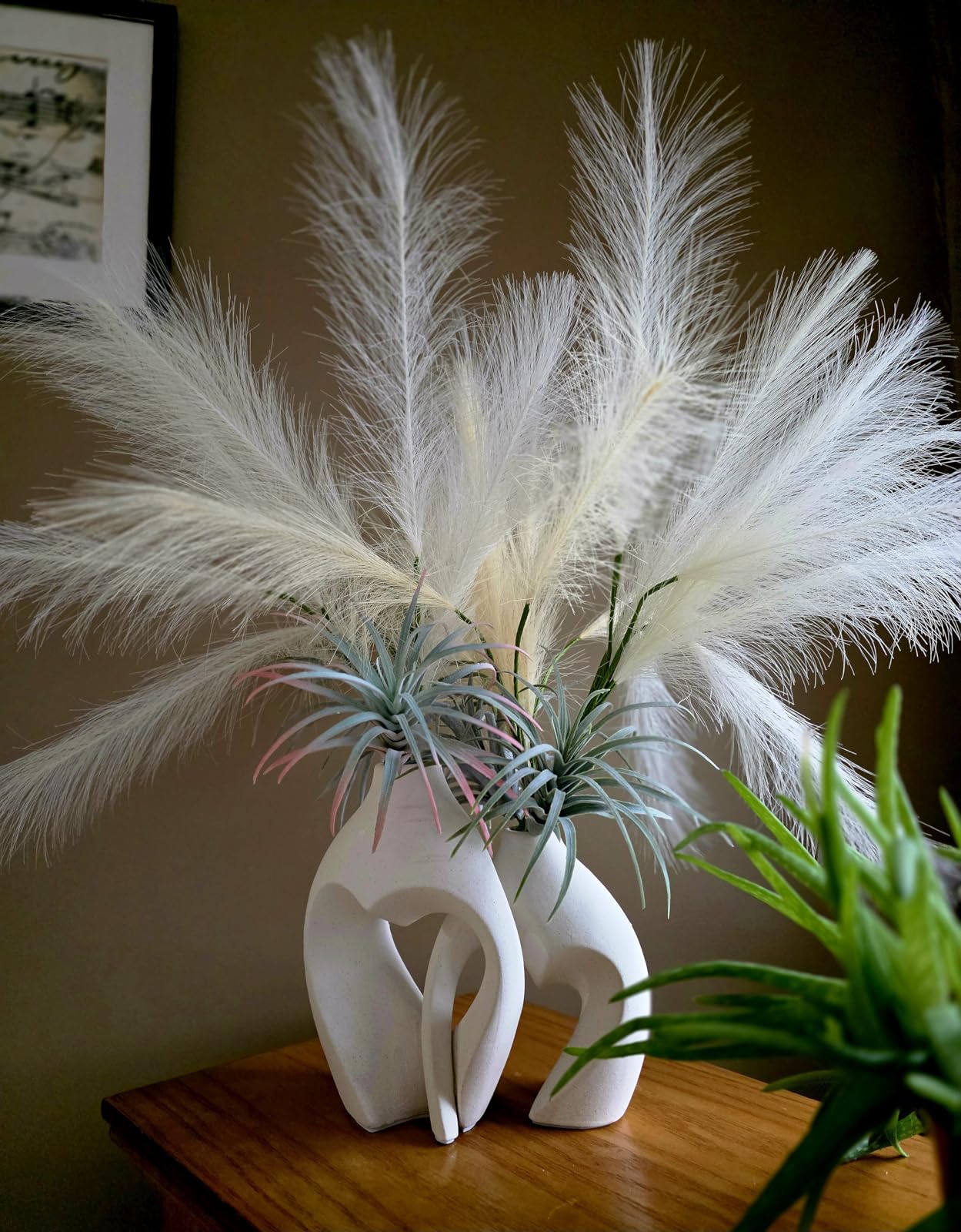 Decorative arrangement with white feathers and air plants in a white vase on a wooden surface.