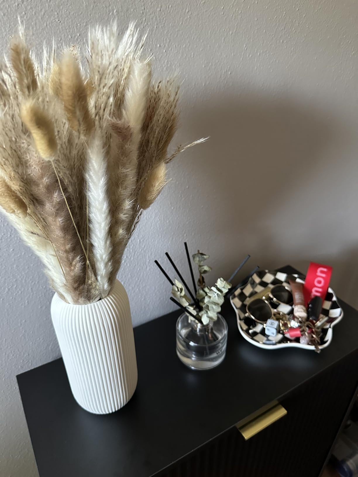 Decorative items including a vase with dried plants, a small glass jar with sticks, and a decorative plate on a dark surface.