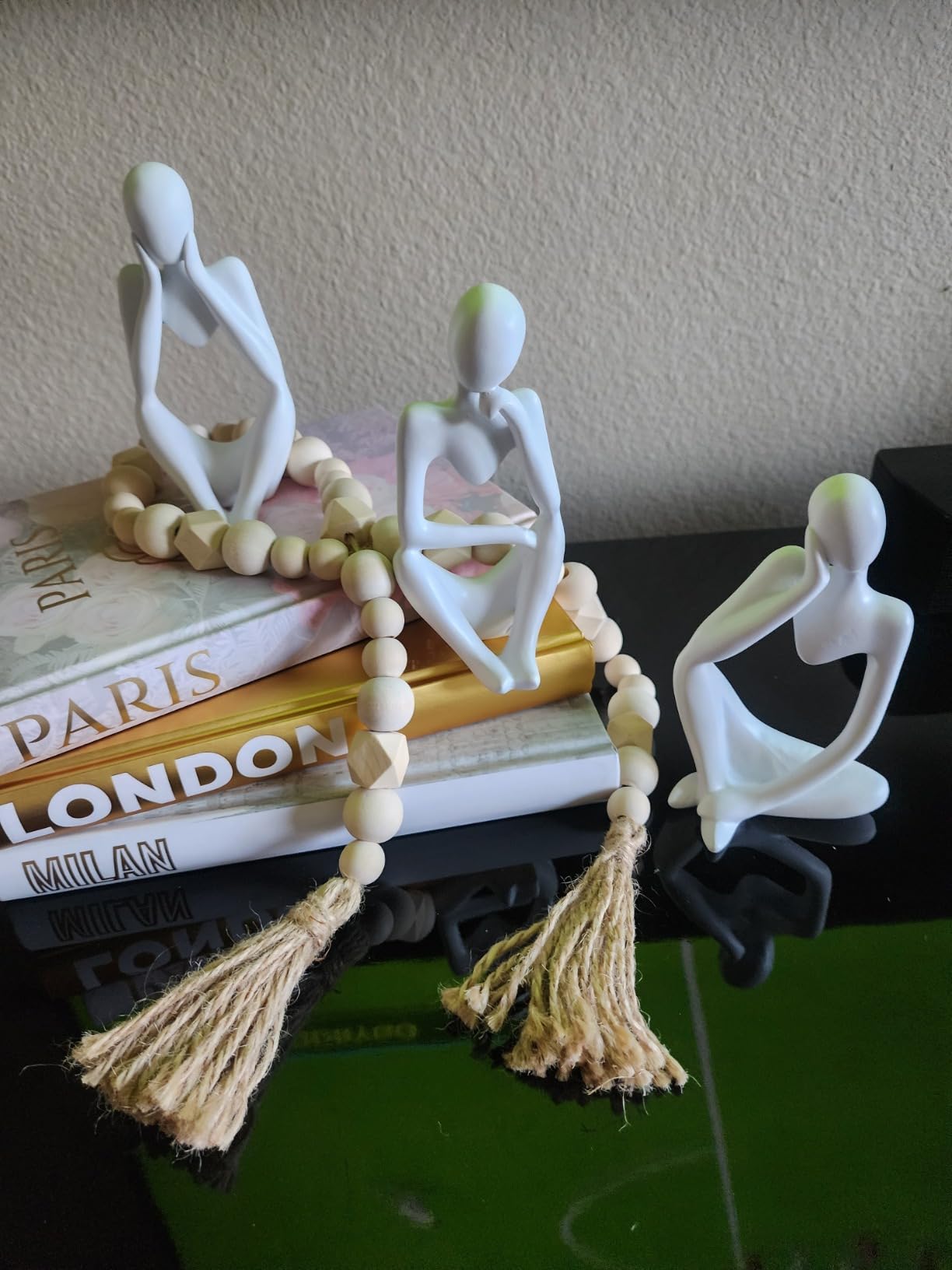 Decorative items with white figures and tassels on books against a plain wall.