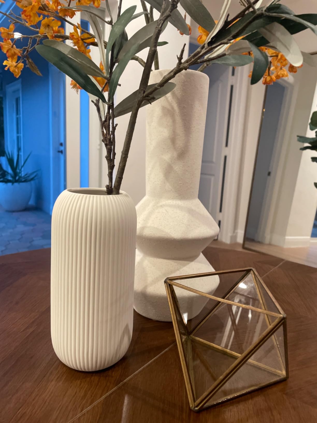 Decorative scene with a textured white vase, geometric glass container, and plant on a wooden surface.