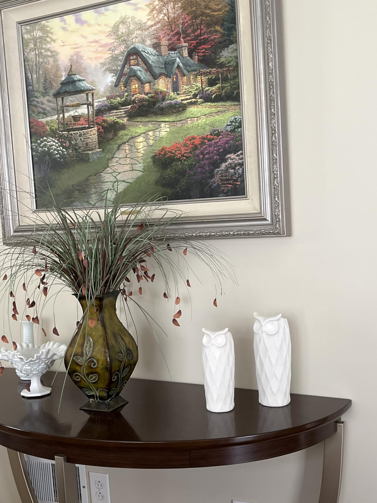 Decorative shelf with vases and a painting of a cottage scene on the wall.