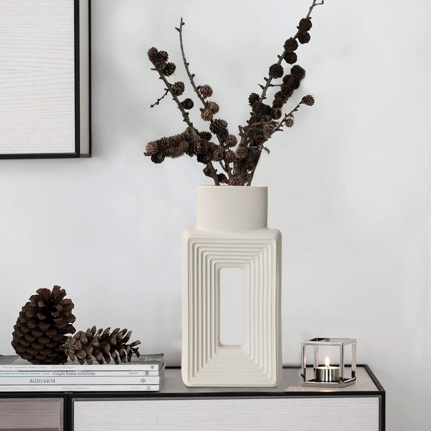 Decorative vase with dried branches on a table against a light wall.