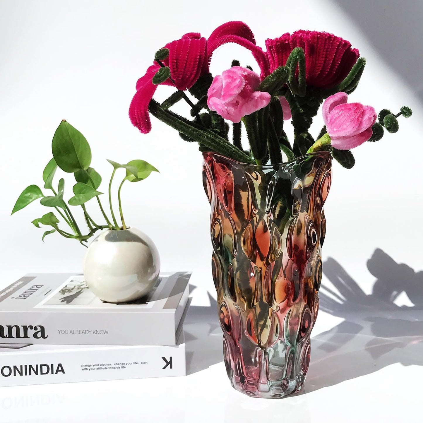 Decorative vase with pink flowers and a small plant on a white surface