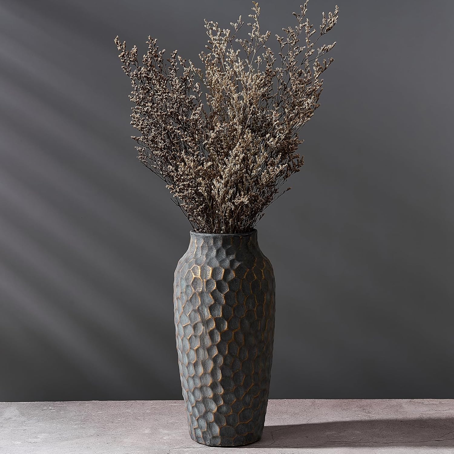 Decorative vase with textured surface holding dried plants against a dark gray background