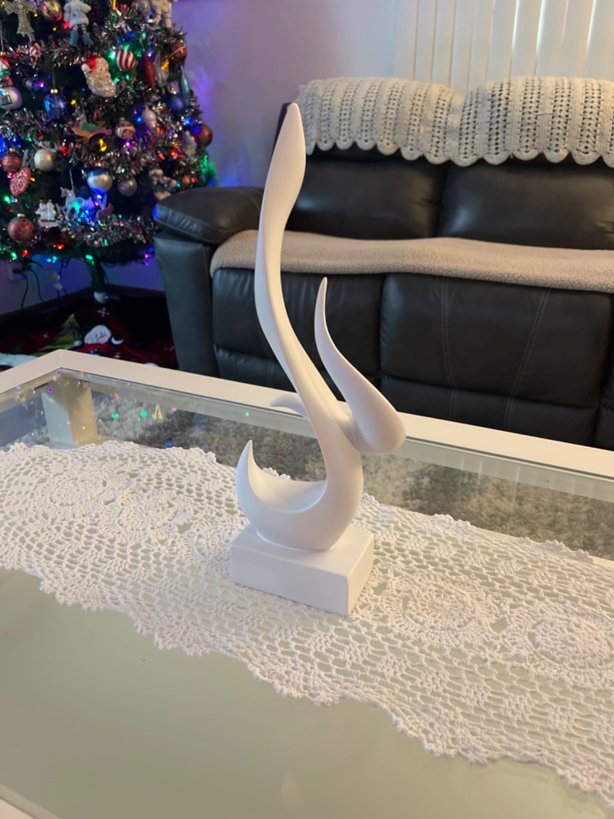 Decorative white sculpture on a glass table with a Christmas tree and black sofa in the background