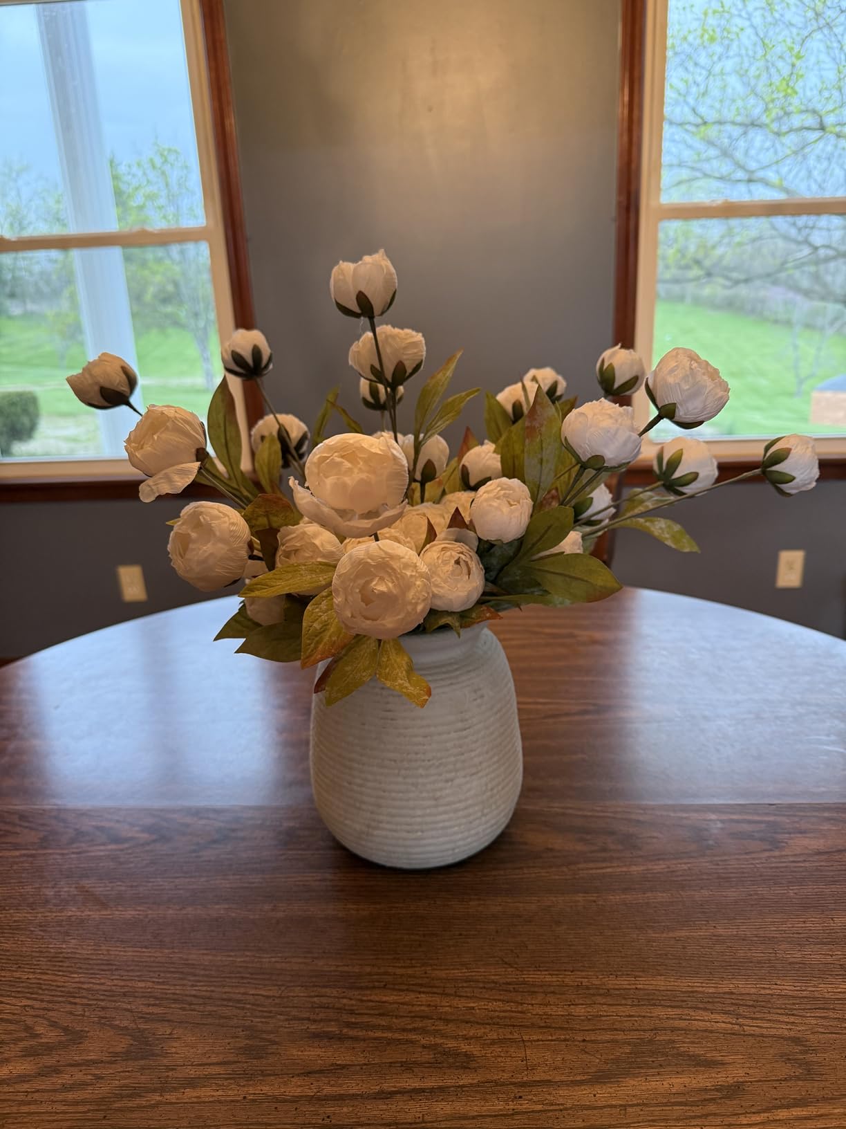 Faux floral arrangement in a vase on a wooden table with a window in the background