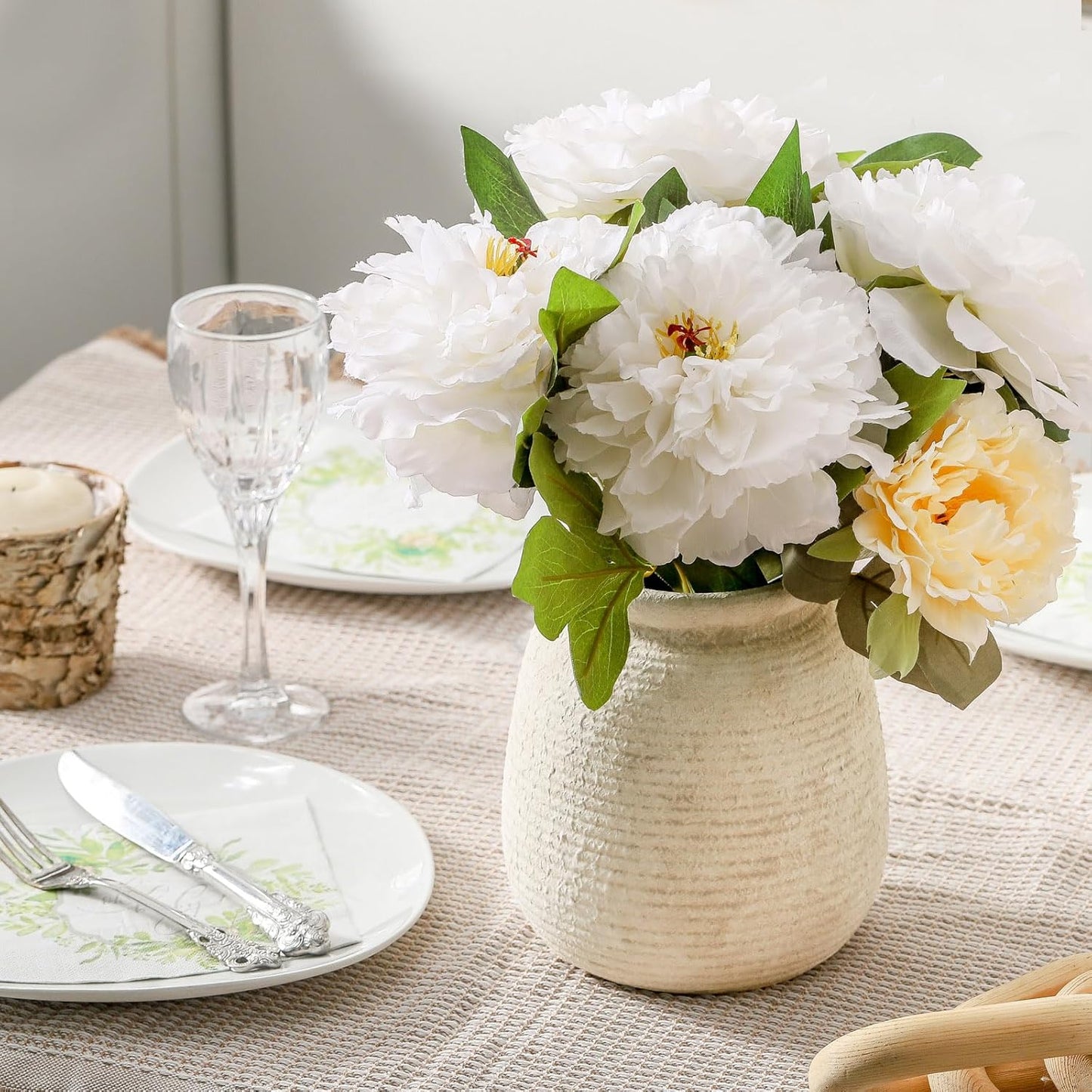 Floral arrangement in a textured vase on a table setting with plates and glasses.