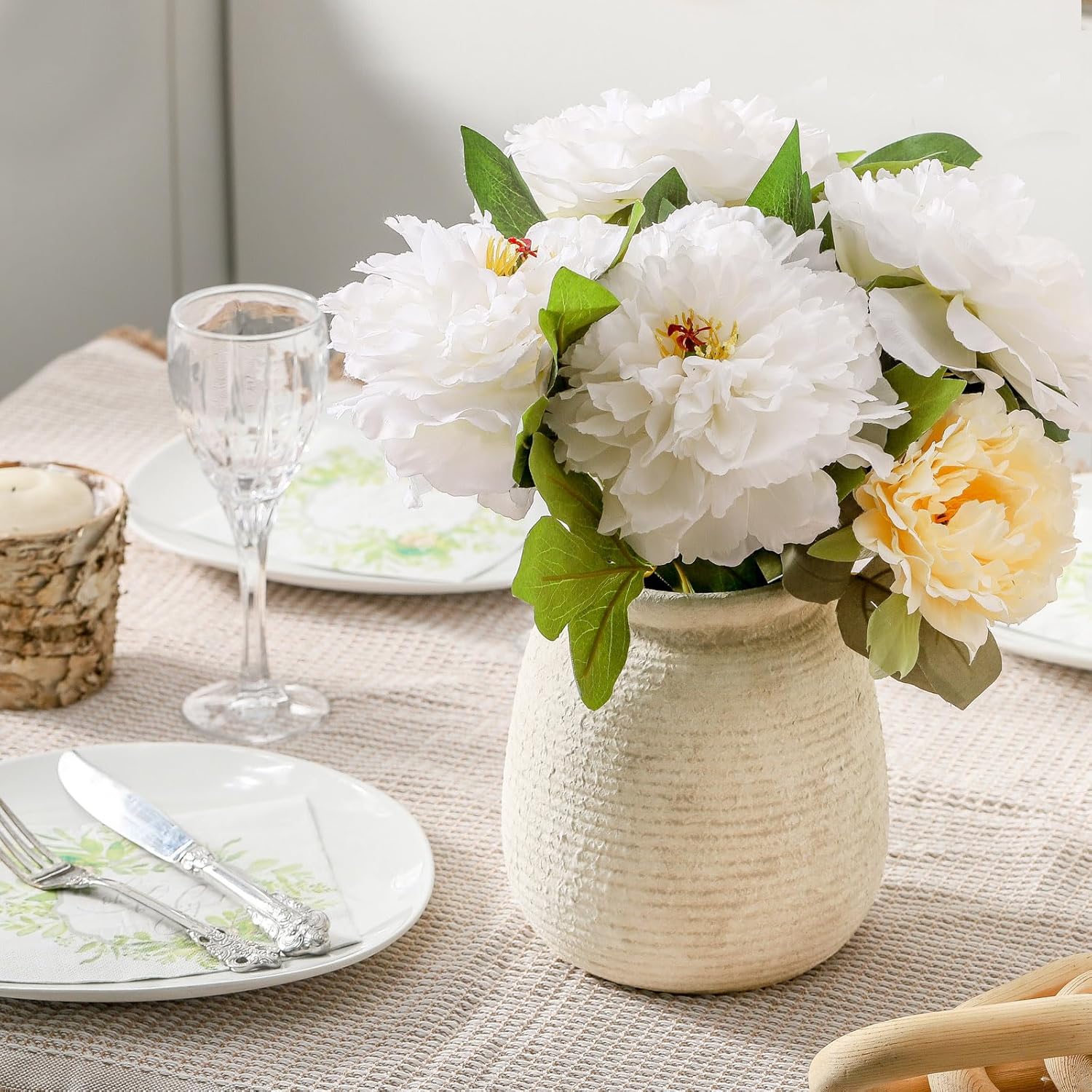 Floral arrangement in a textured vase on a table setting with plates and glasses.