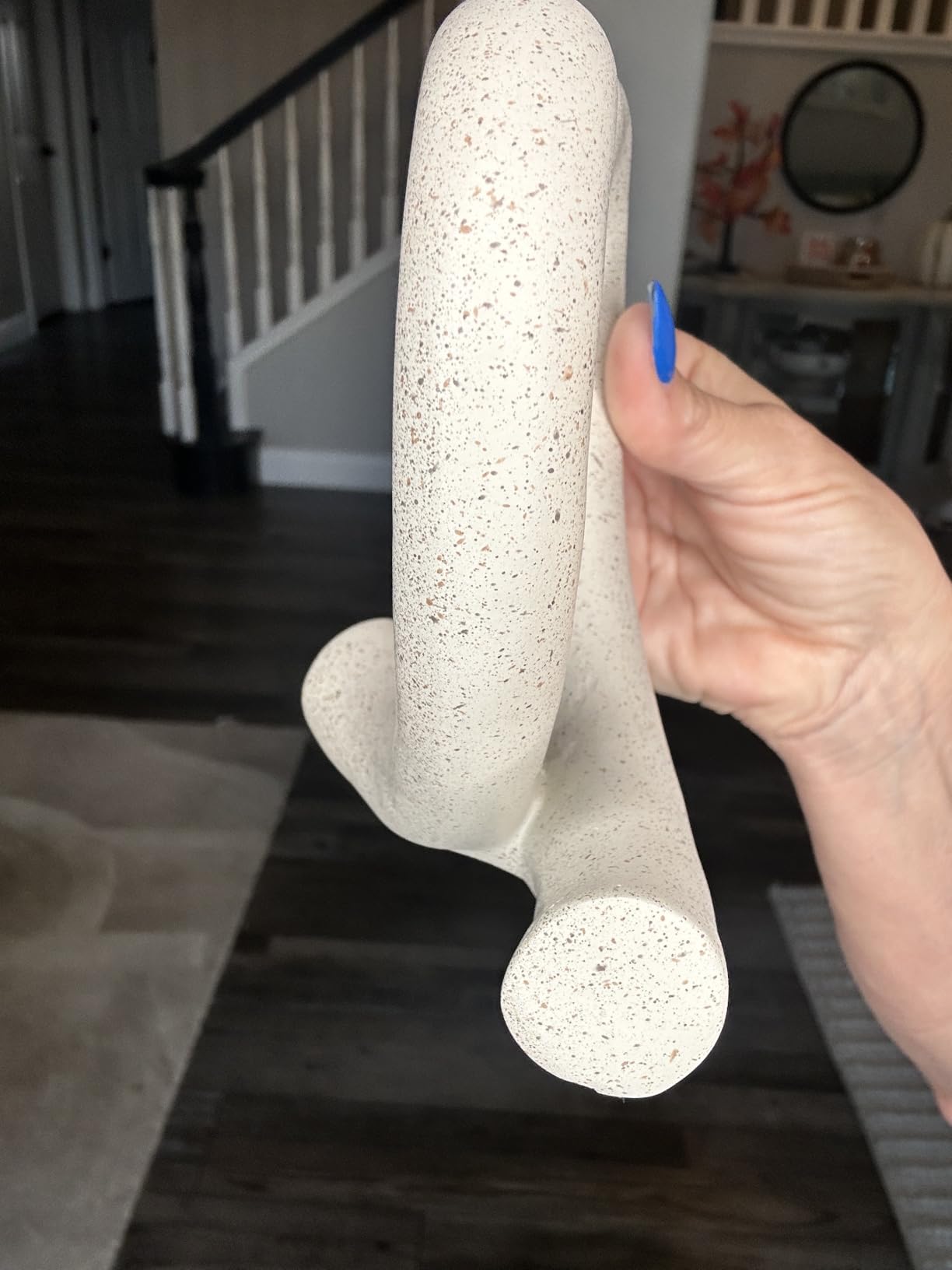 Hand holding a textured white object indoors with a staircase in the background