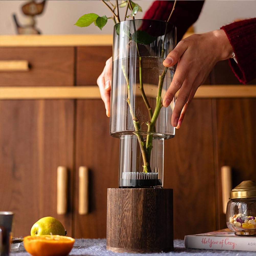 Person holding a clear vase with a plant, wooden cabinet in the background