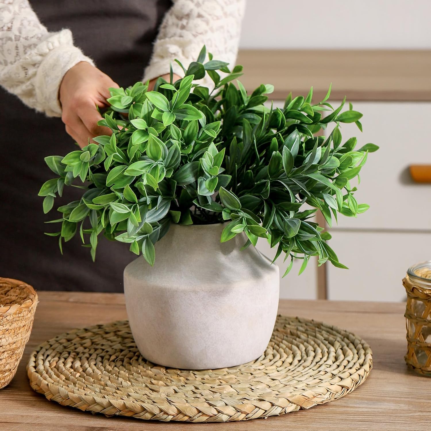 Person holding a potted plant on a wooden table with a woven mat