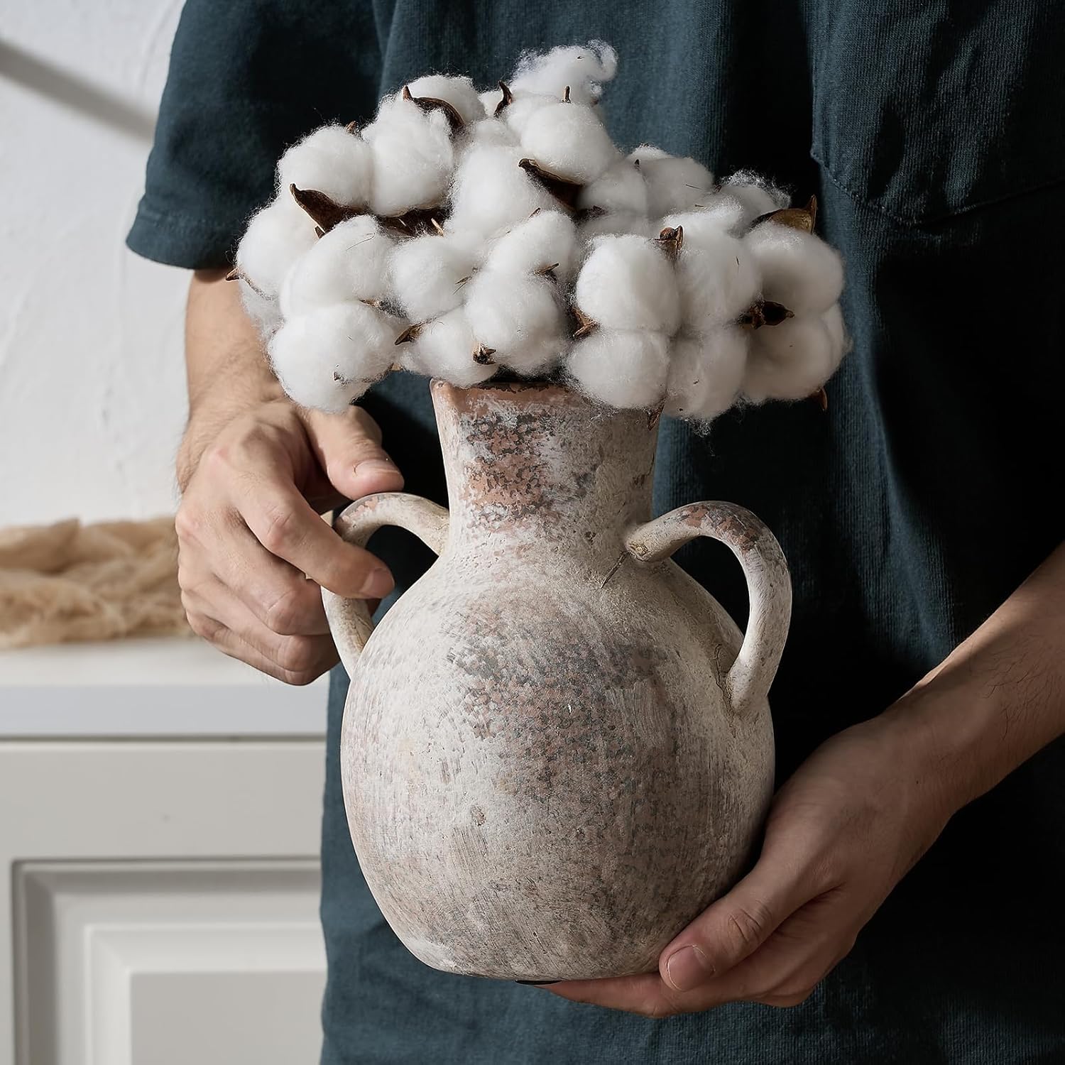 Person holding a textured vase with cotton in a neutral setting