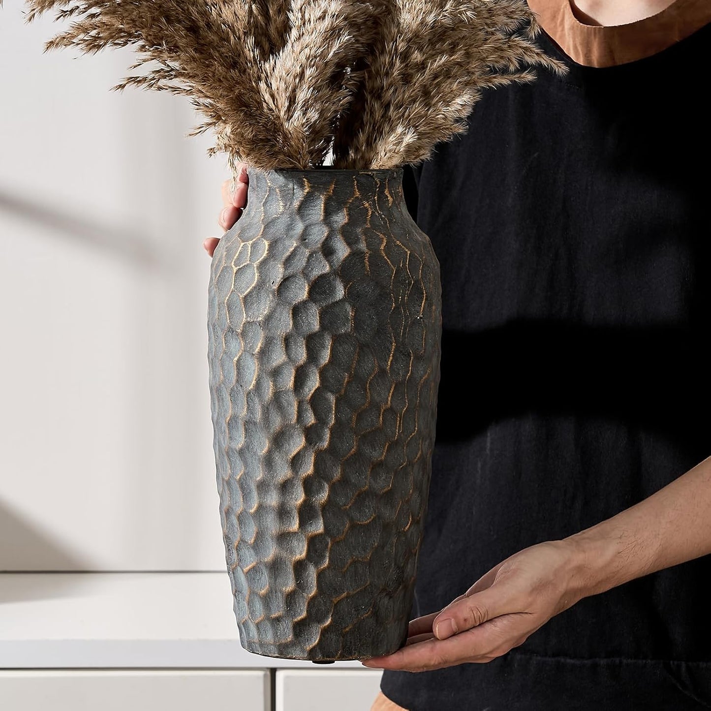 Person holding a textured vase with dried plants against a neutral background