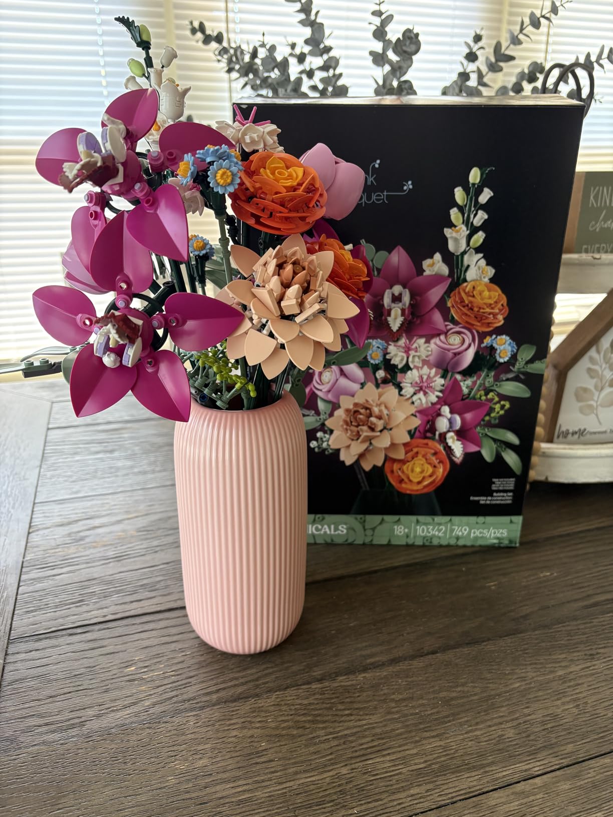 Pink vase with flowers on a wooden surface next to a magazine with floral design