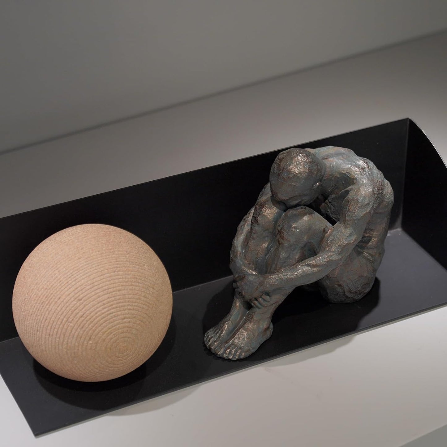 Sculpture of a person sitting next to a sphere on a black platform.