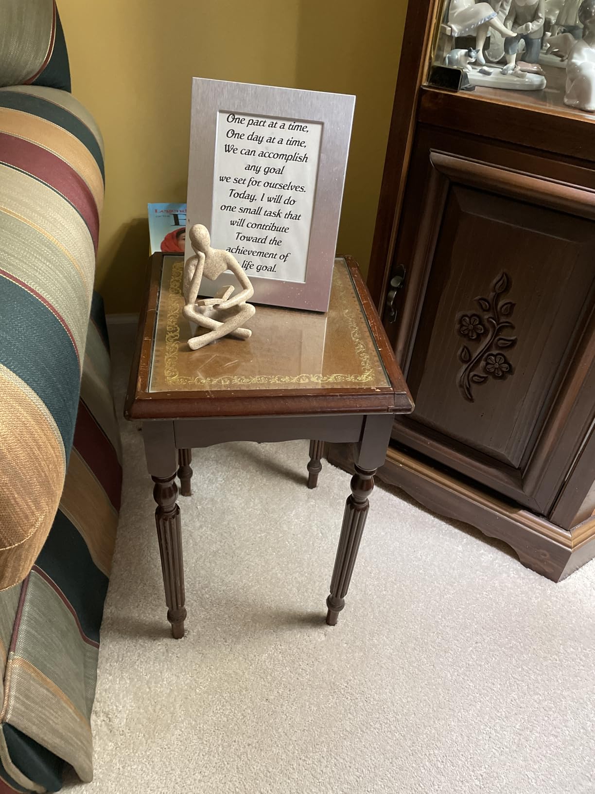 Small wooden table with a framed quote and decorative item against a wall.