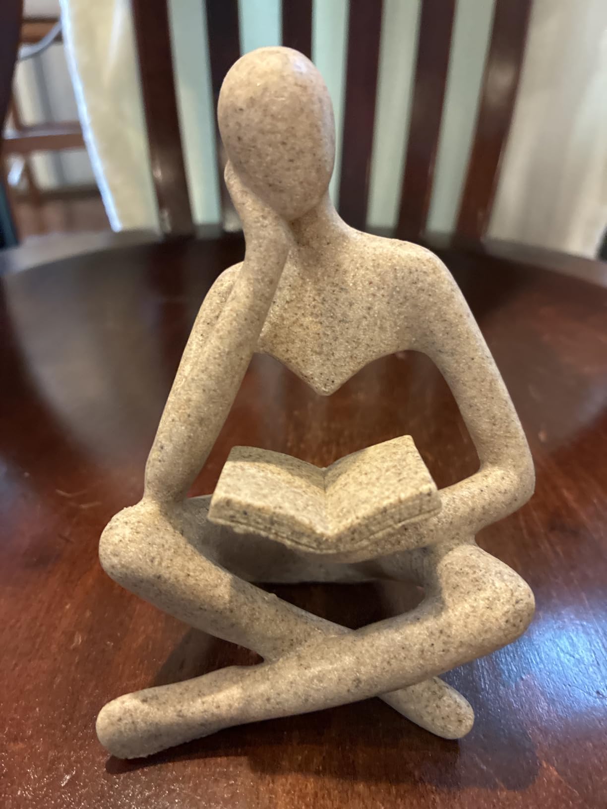 Statue of a person sitting and reading a book on a wooden surface