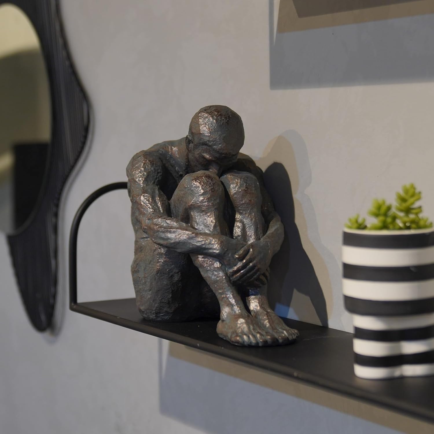 Statue of a person sitting on a shelf with a plant in the background