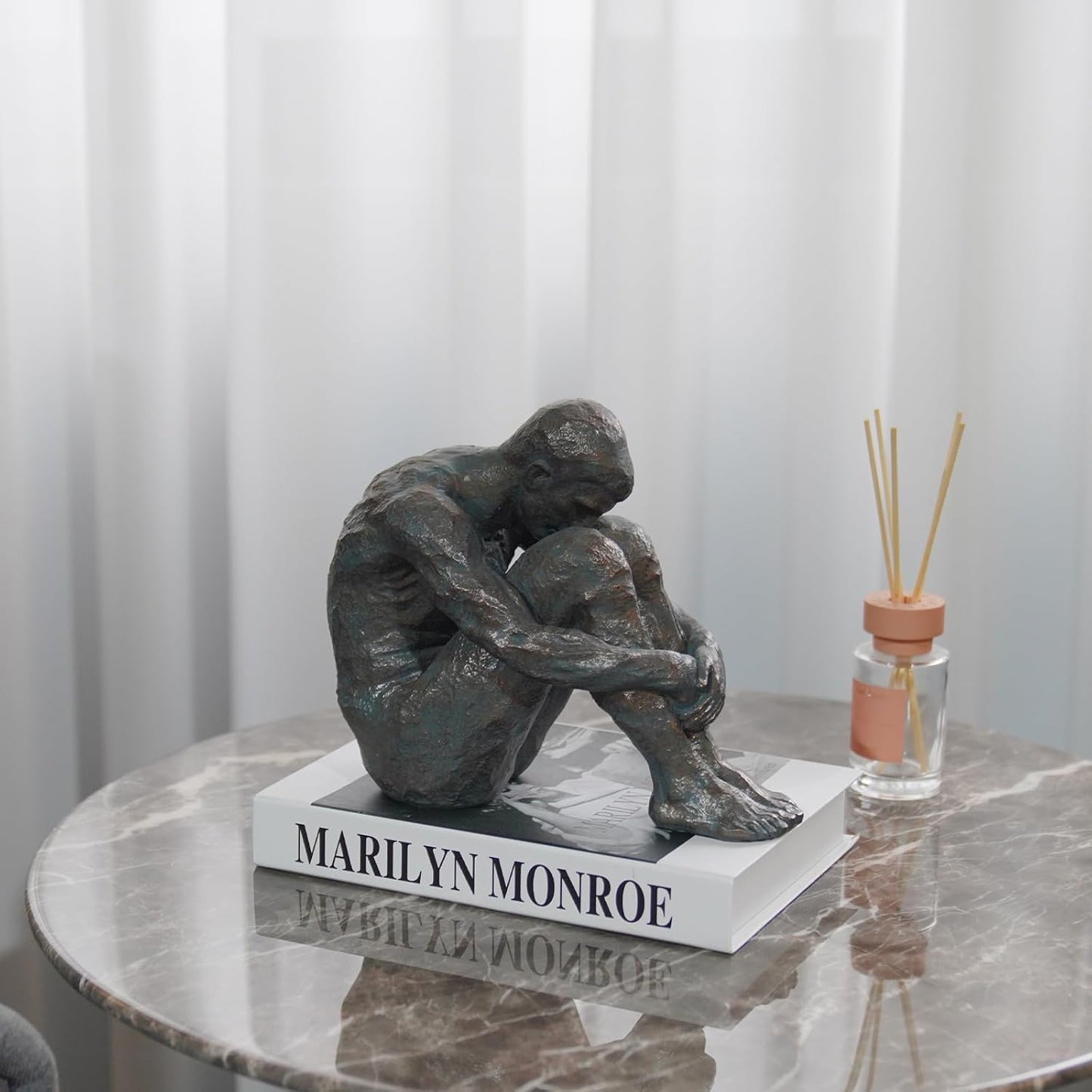Statue of a sitting figure on a marble table with 'Marilyn Monroe' text