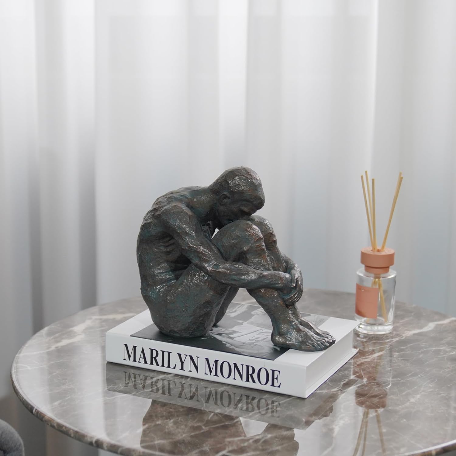 Statue of a sitting figure on a marble table with 'Marilyn Monroe' text