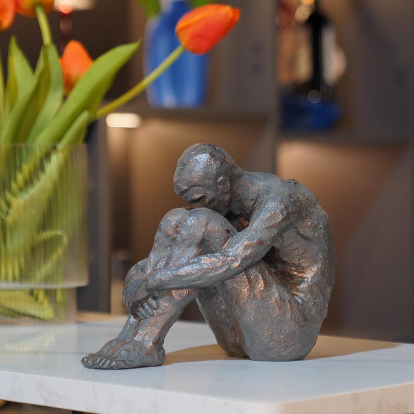 Statue of a sitting figure on a table with flowers in the background