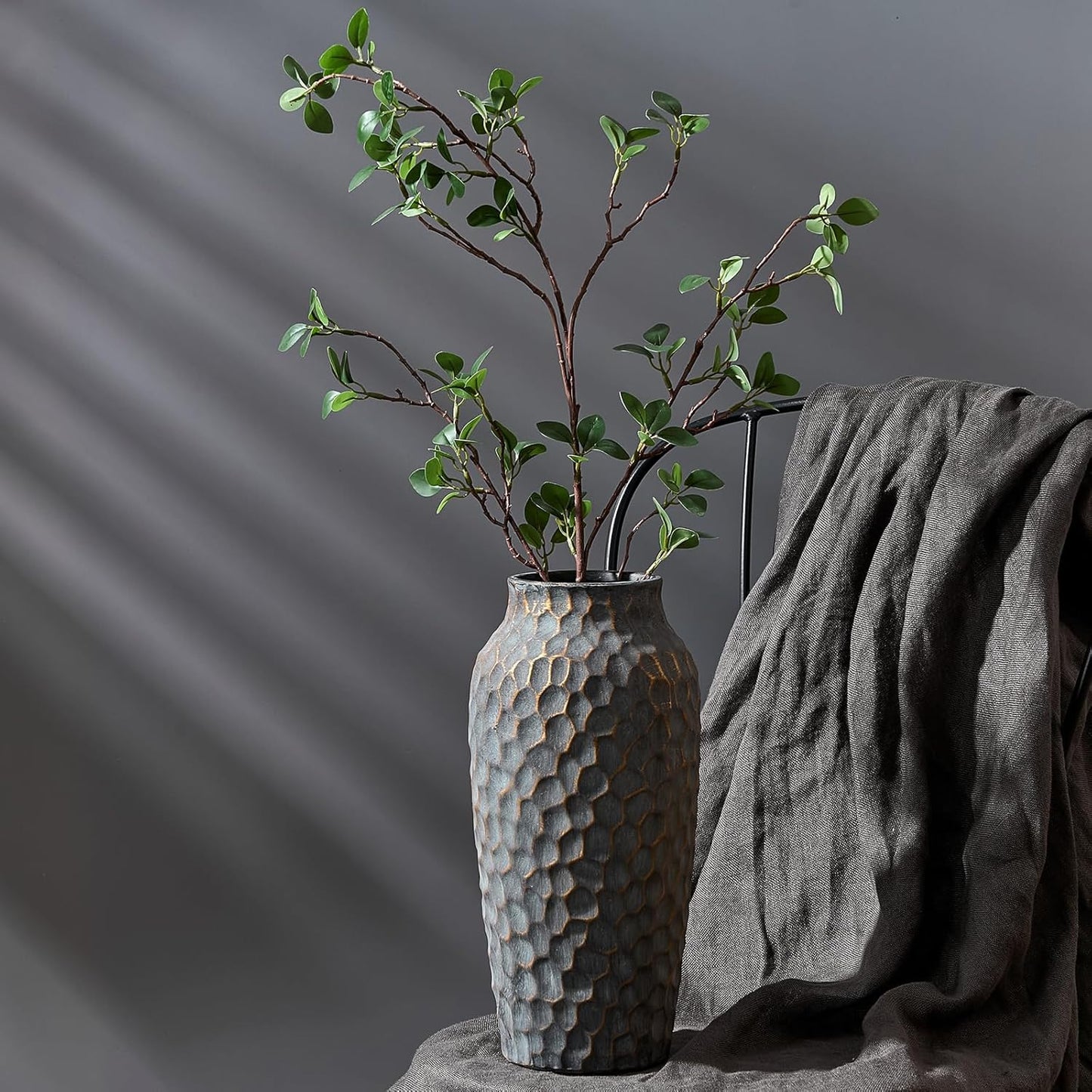 Textured vase with green branches on a gray surface