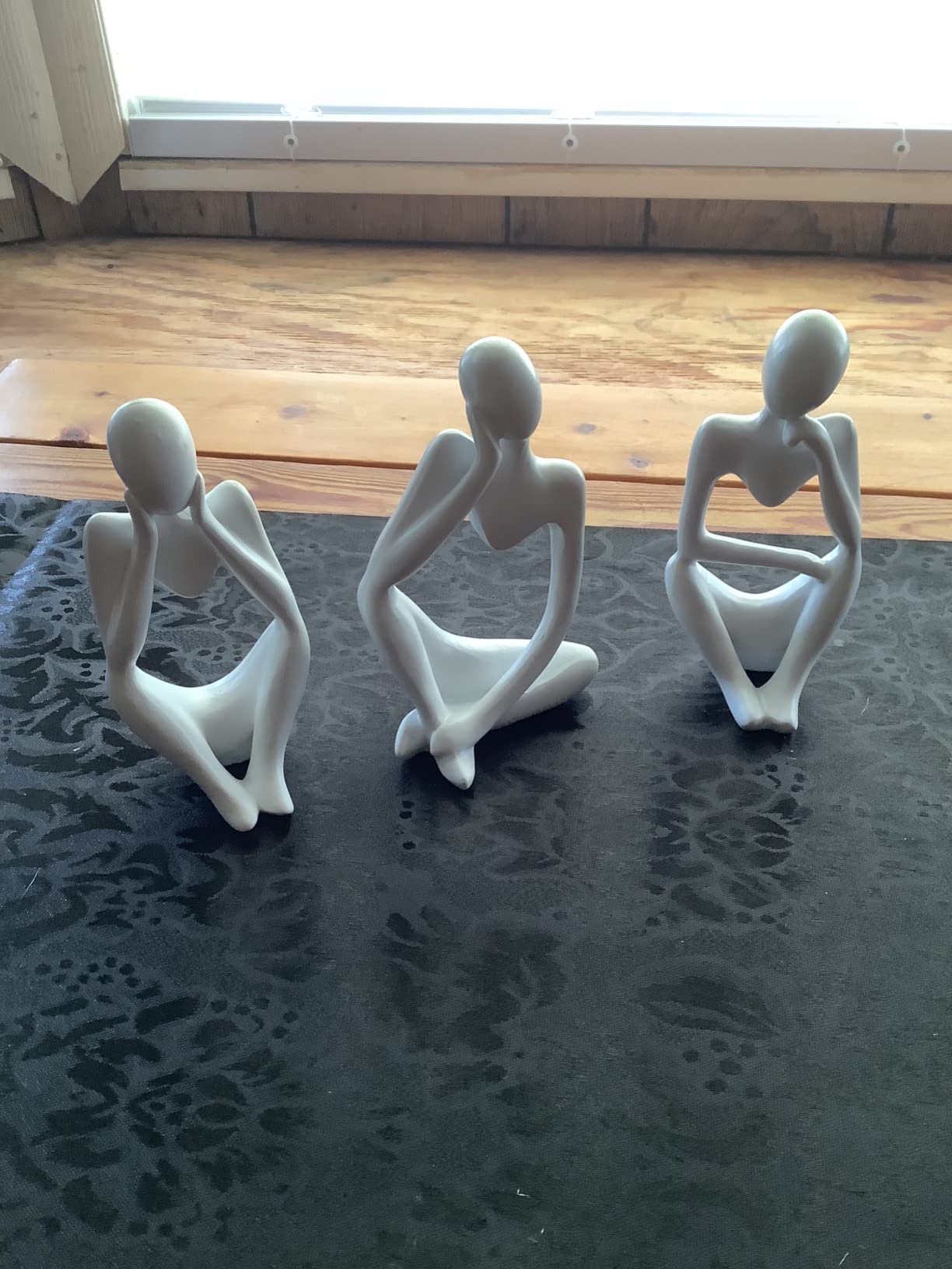 Three white abstract figurines on a textured surface with a wooden floor in the background.