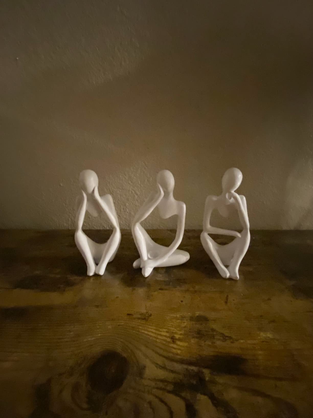 Three white ceramic figures on a wooden surface with a neutral background