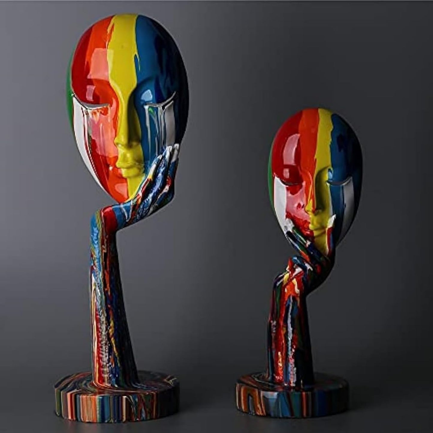 Two colorful abstract sculptures of faces on stands against a dark background