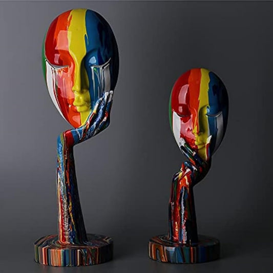 Two colorful abstract sculptures of faces on stands against a dark background